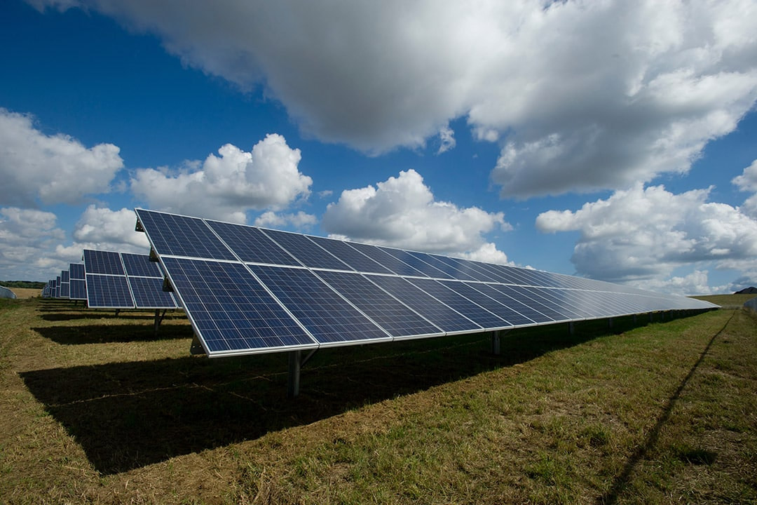 Mehrere Solarmodule auf einer Freifläche unter blauem Himmel mit großen Wolken.