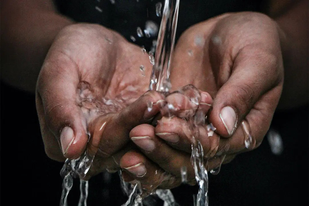 Zwei Hände formen eine Schale, in die von oben ein Wasserstrahl fließt.