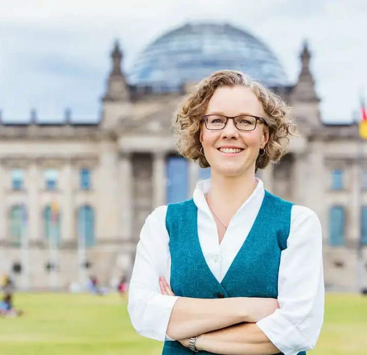 Julia Verlinden mit verschränkten Armen vor dem Reichstagsgebäude mit der Glaskuppel des Deutschen Bundestags im Hintergrund.